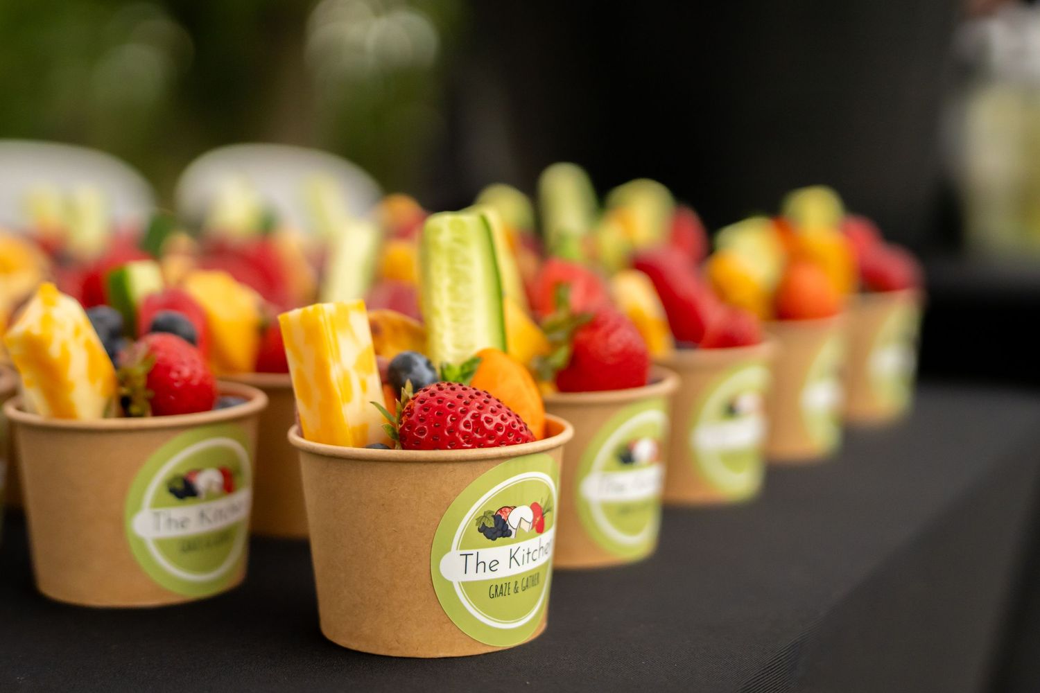 Fresh fruit cups with strawberries, mango, and blueberries arranged in a row at an outdoor event.