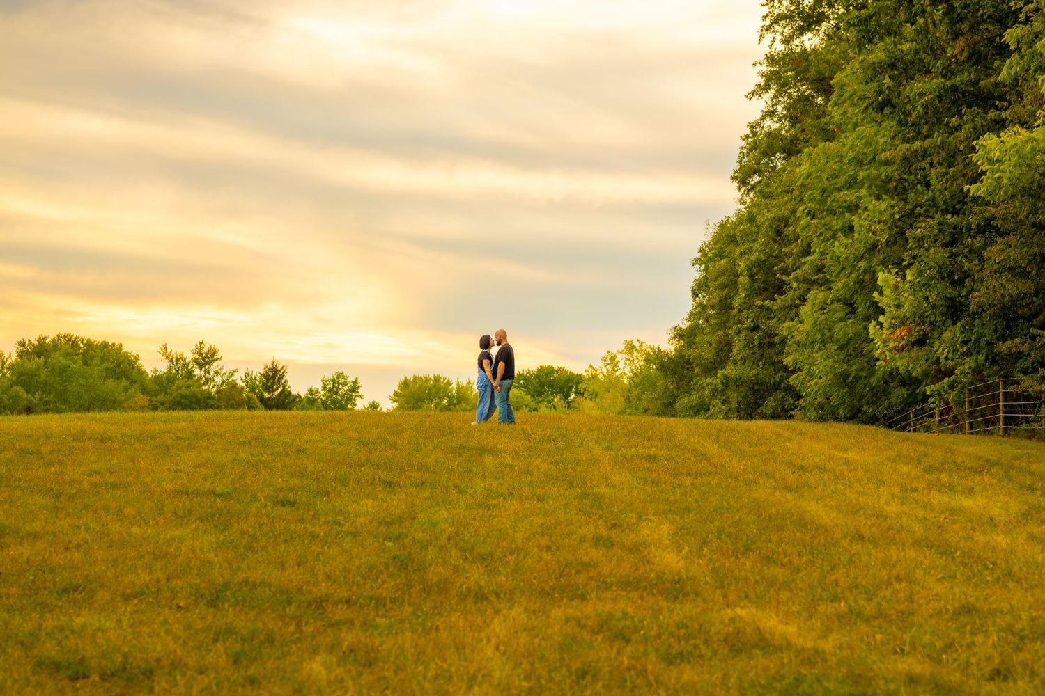 Couple embracing on a vast green hillside under a dramatic golden sunset sky.