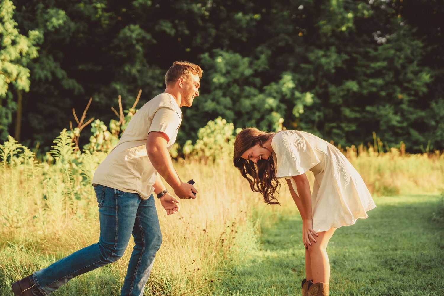 Excited couple sharing a joyful moment on a sunlit meadow path after a marriage proposal.