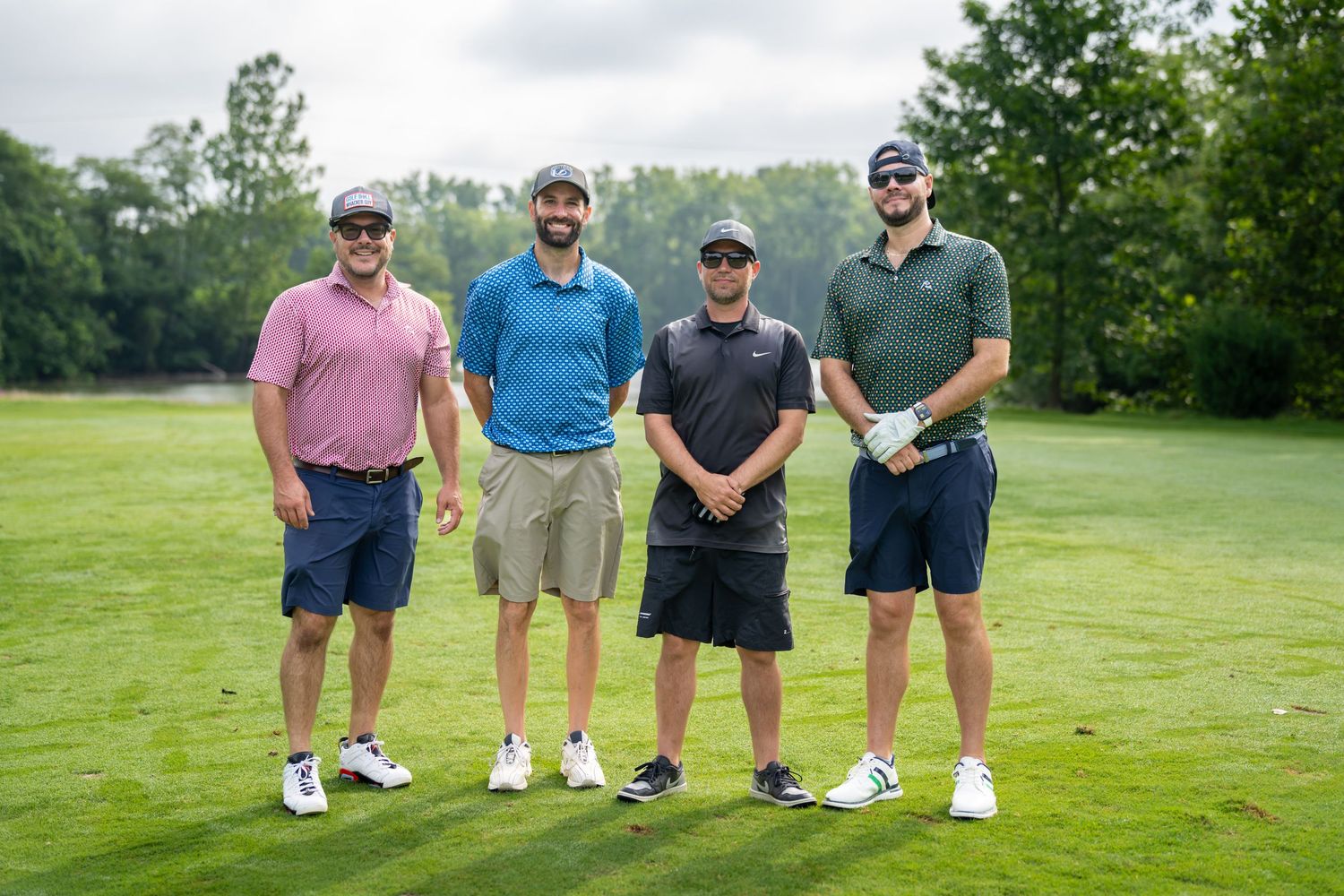 Four men smiling and posing together on a lush green golf course during a golf tournament.
