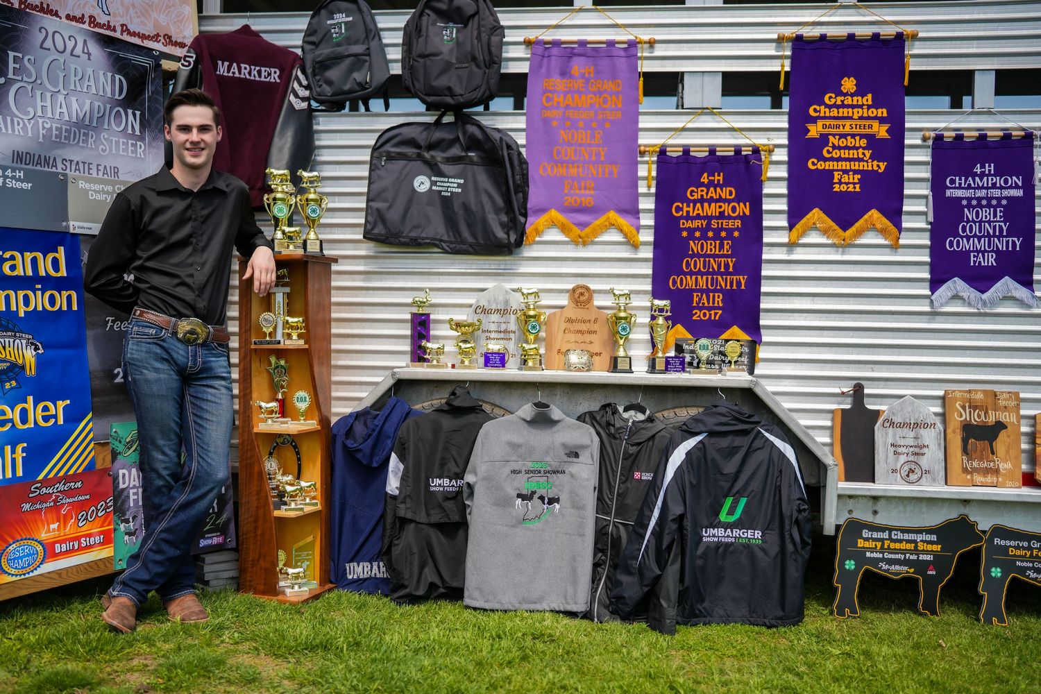 Young man standing beside champion banners, trophies, and jackets at a livestock show.
