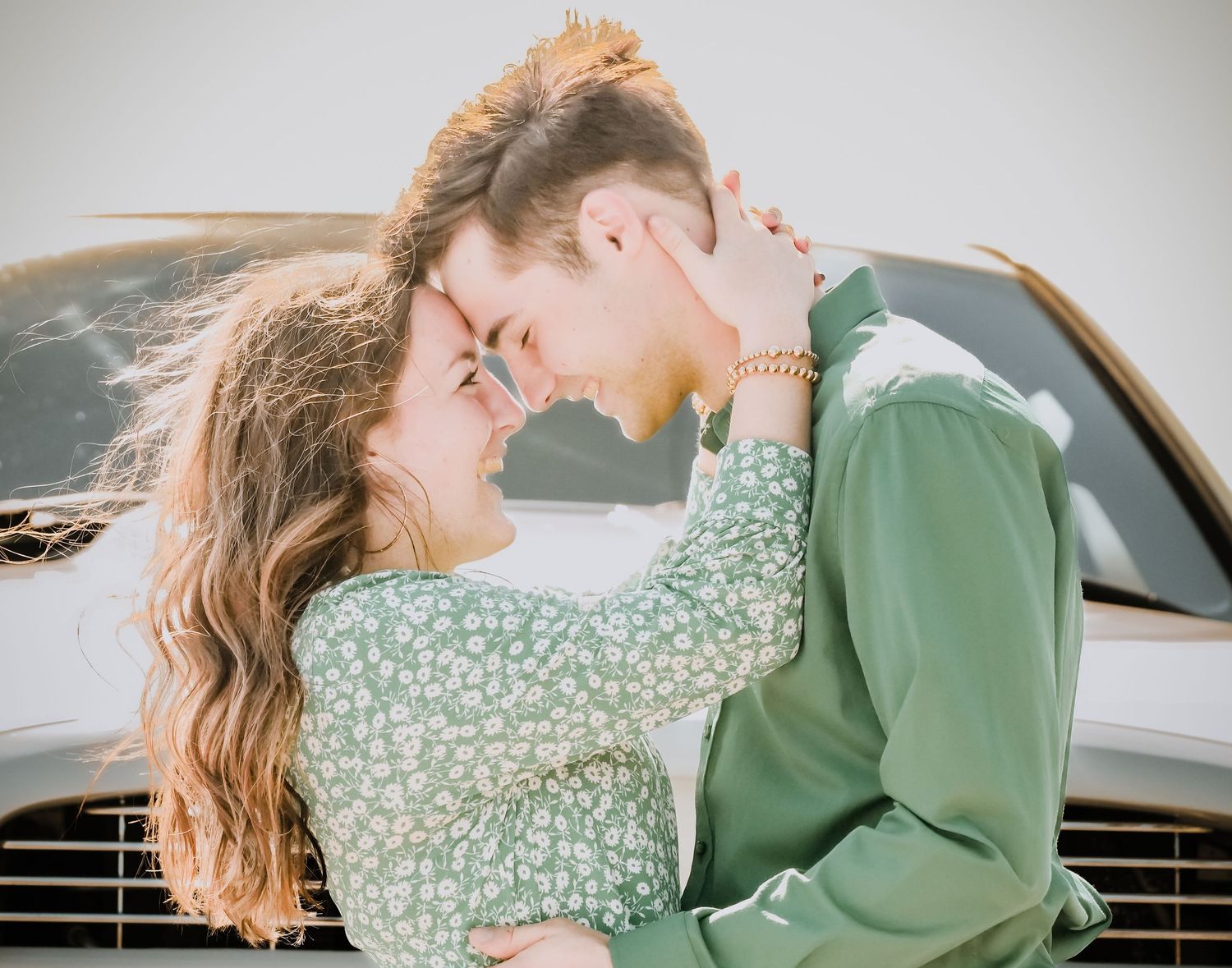 Loving couple in green outfits sharing an intimate moment leaning foreheads together near a white vehicle.