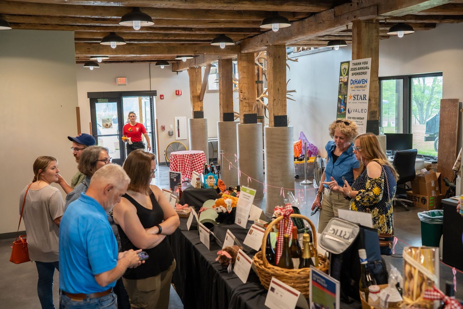 Guests browsing silent auction items and gift baskets inside a rustic barn venue during a charity fundraiser event.
