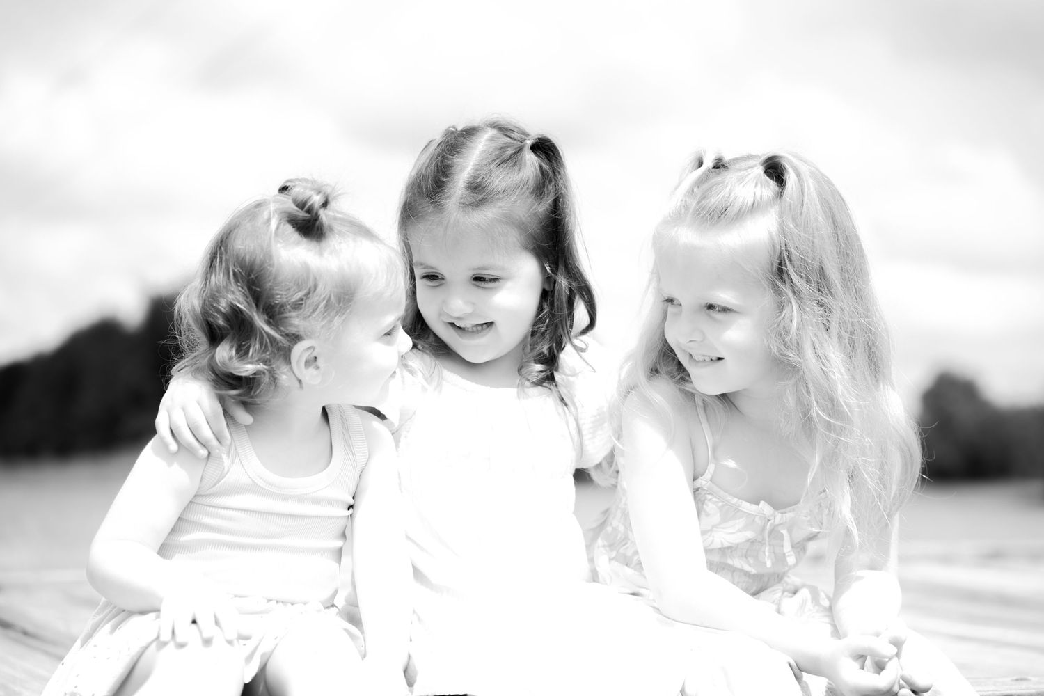 Three young girls smiling and laughing together outdoors in a black and white portrait photo.