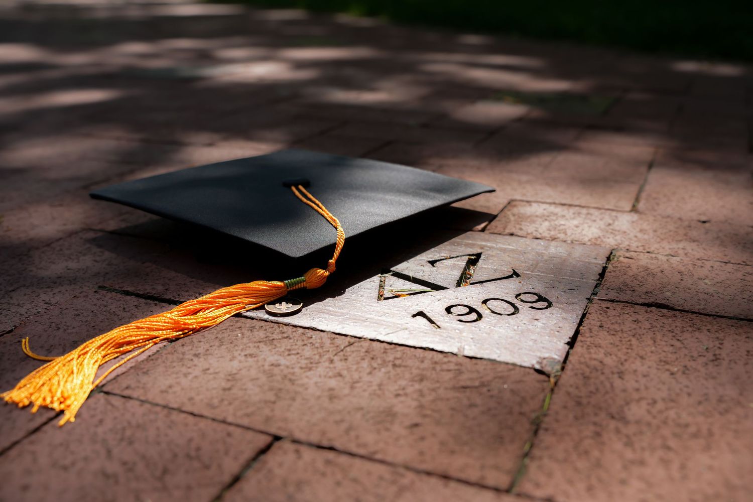Graduation cap with gold tassel resting on brick pavement engraved with Delta Zeta 1909.