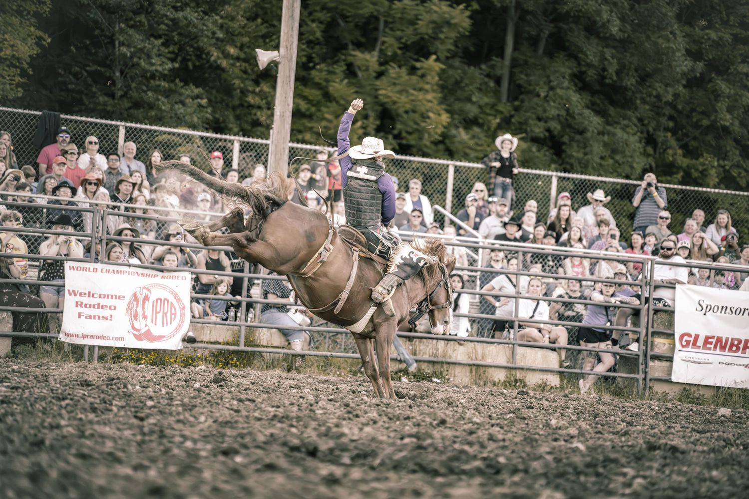 Rodeo cowboy riding a bucking bull at an ABP event with a large crowd of spectators cheering in stands.