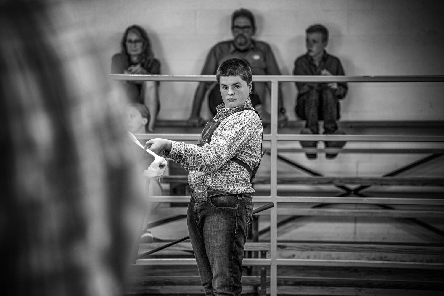 Young man in plaid shirt holds papers while standing at an indoor livestock judging event.