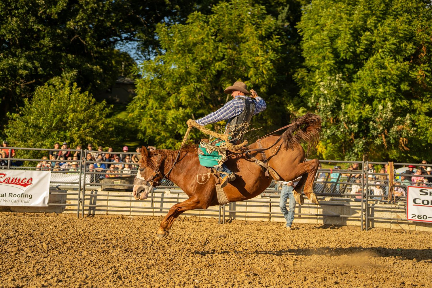 A cowboy rides a fast chestnut horse while roping at a sunny outdoor rodeo competition.