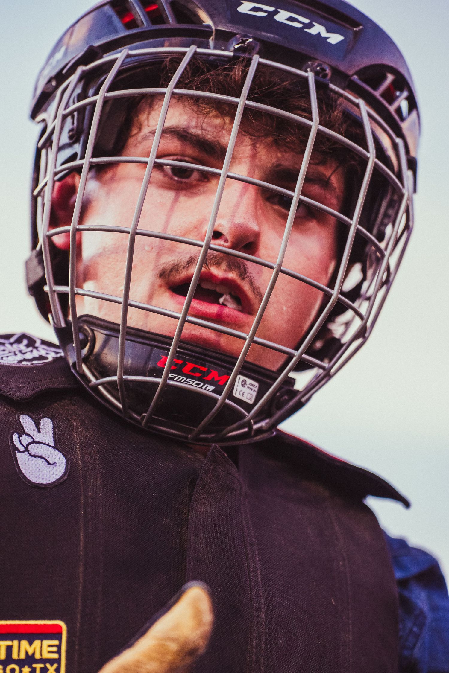 A young hockey player wearing a CCM helmet with a cage face guard and chest protector looks intensely at the camera.