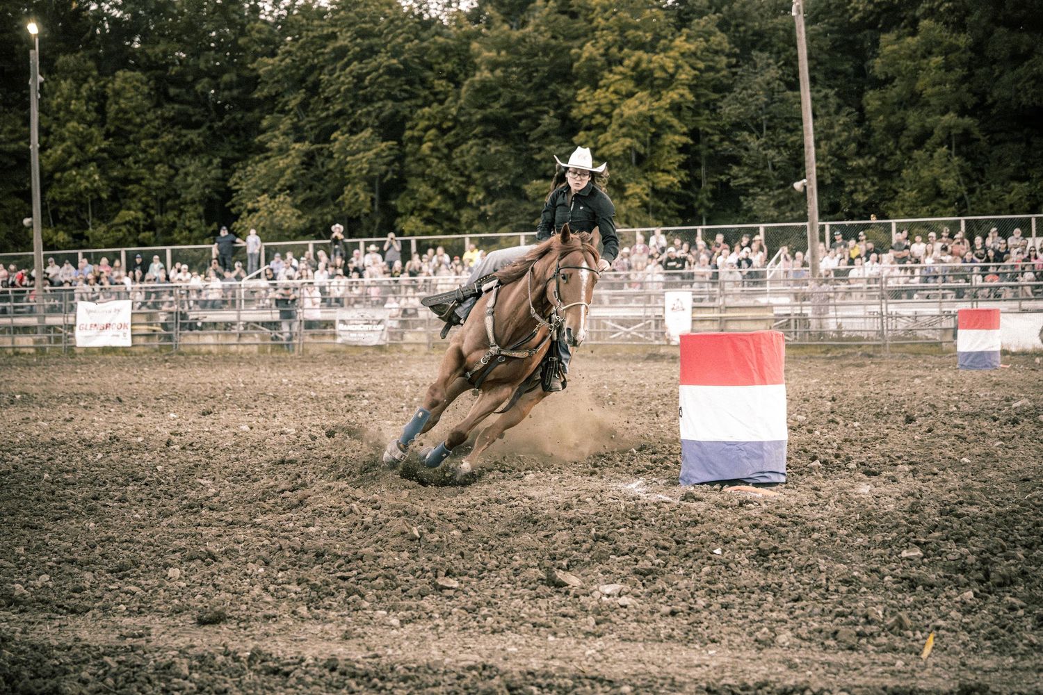 Cowboy on horseback rounds a barrel during a barrel racing competition at an outdoor rodeo arena.