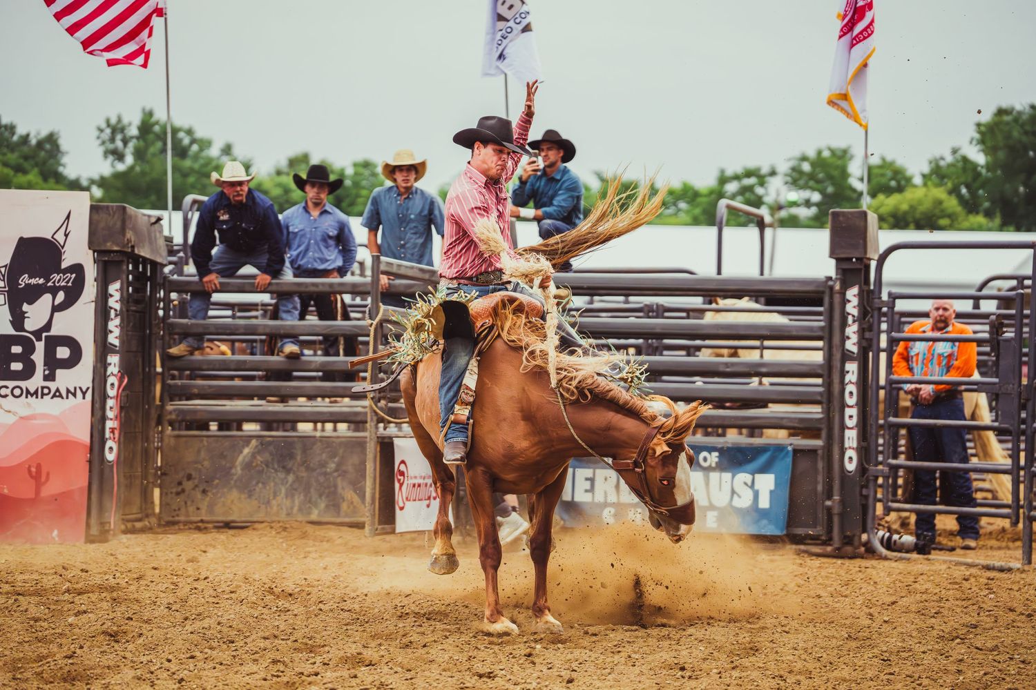 Cowboy riding a bucking bronco at a rodeo competition with spectators watching in the background.