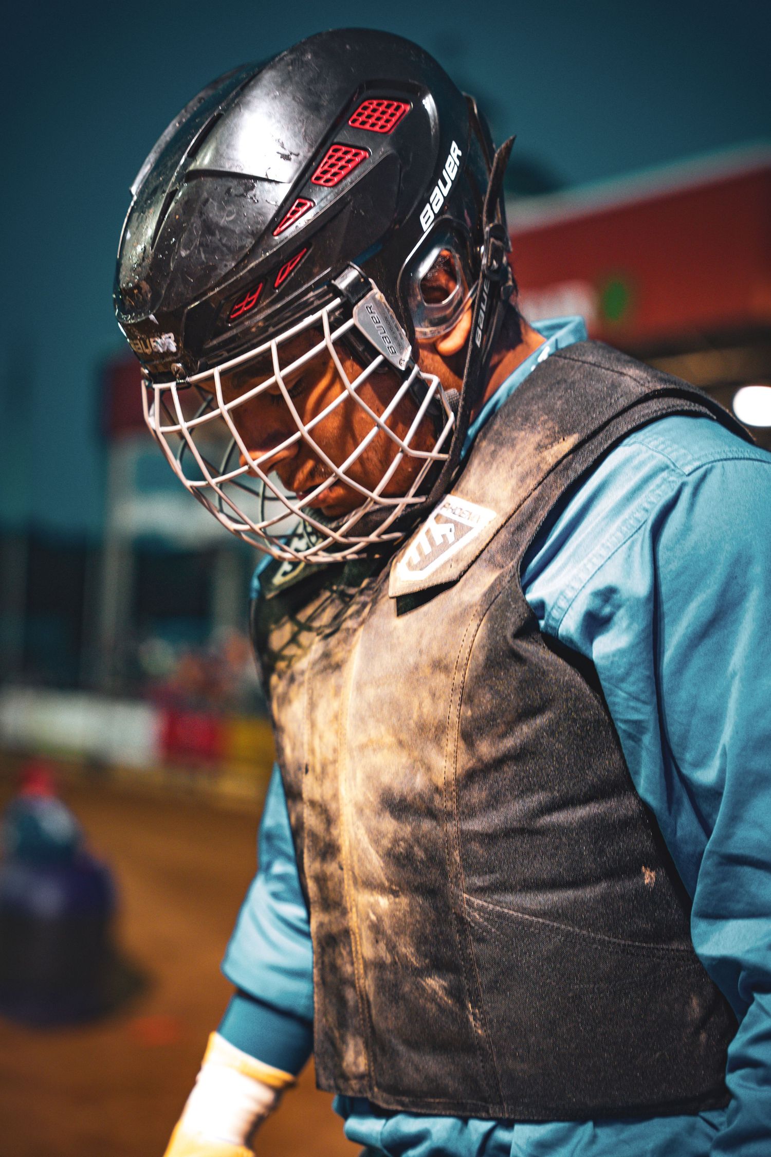 Rodeo bullfighter wearing a dirty protective vest and Bauer helmet with face cage at an arena.