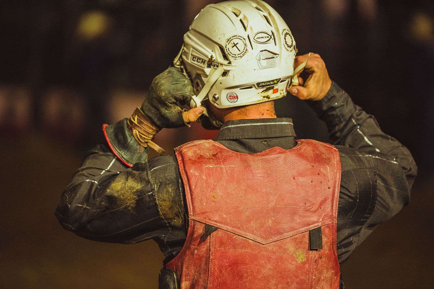 Worker in red vest and white helmet adjusts gear at an industrial site.