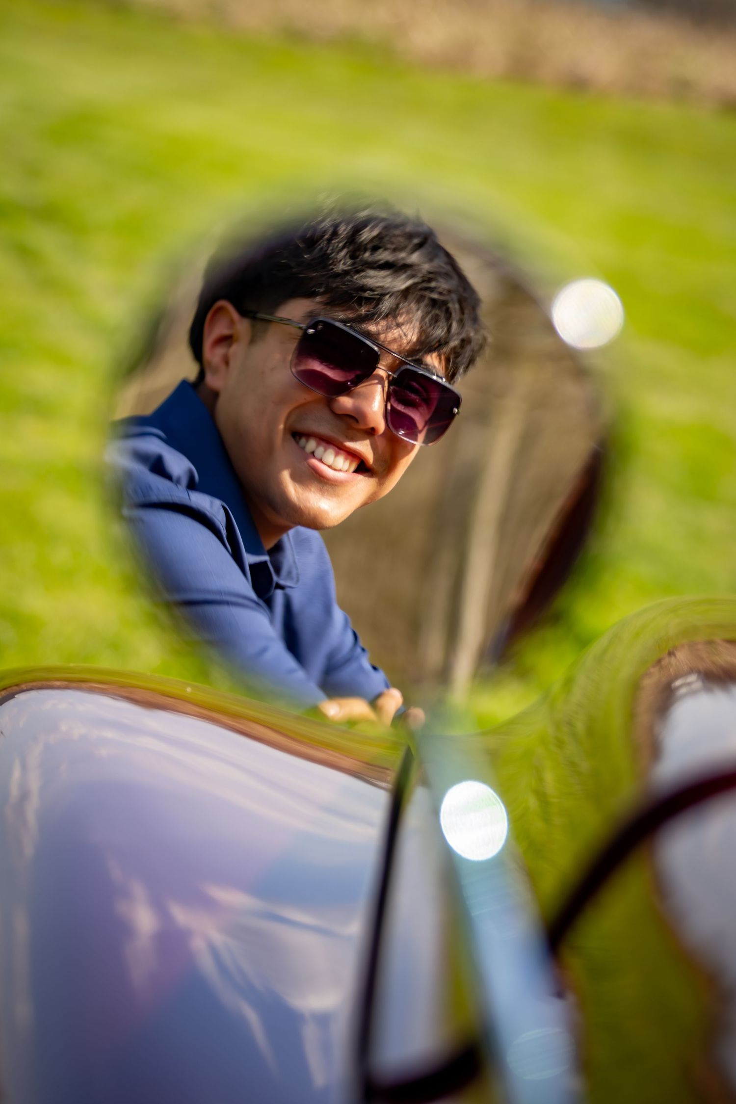 Smiling young man with sunglasses reflected in the side mirror of a vintage red classic truck.