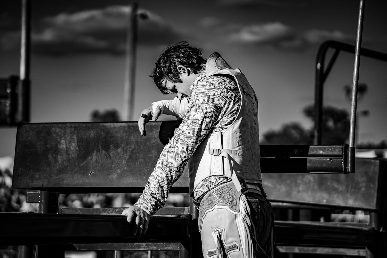 Black and white photo of a rodeo cowboy leaning over a metal chute gate preparing for a bull ride.