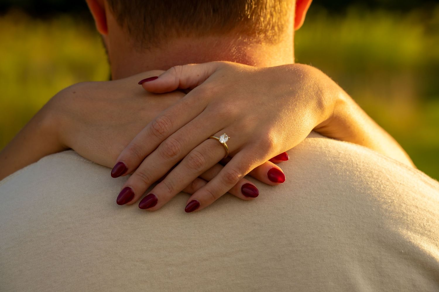 Close-up of a woman's hand with an engagement ring and red nails resting on her partner's shoulder.