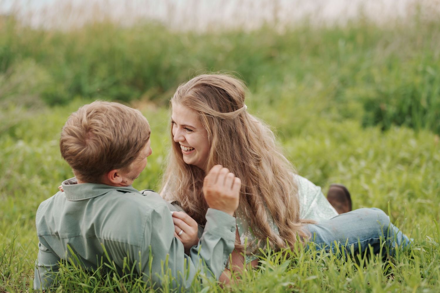 Young couple lying in green grass laughing and enjoying each others company outdoors.