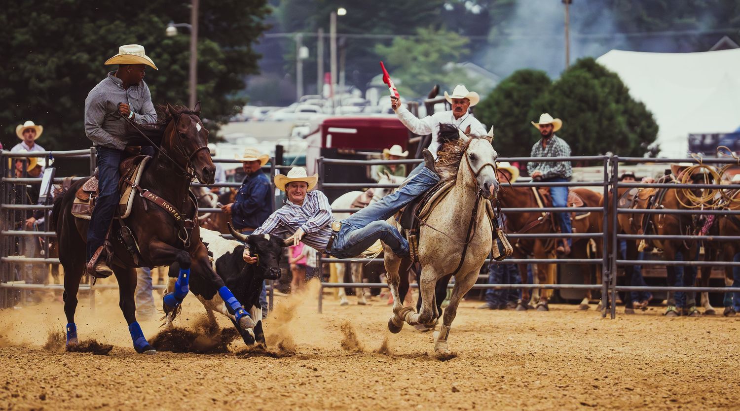 Cowboys compete in a thrilling steer wrestling event at a dusty outdoor rodeo arena with spectators watching.