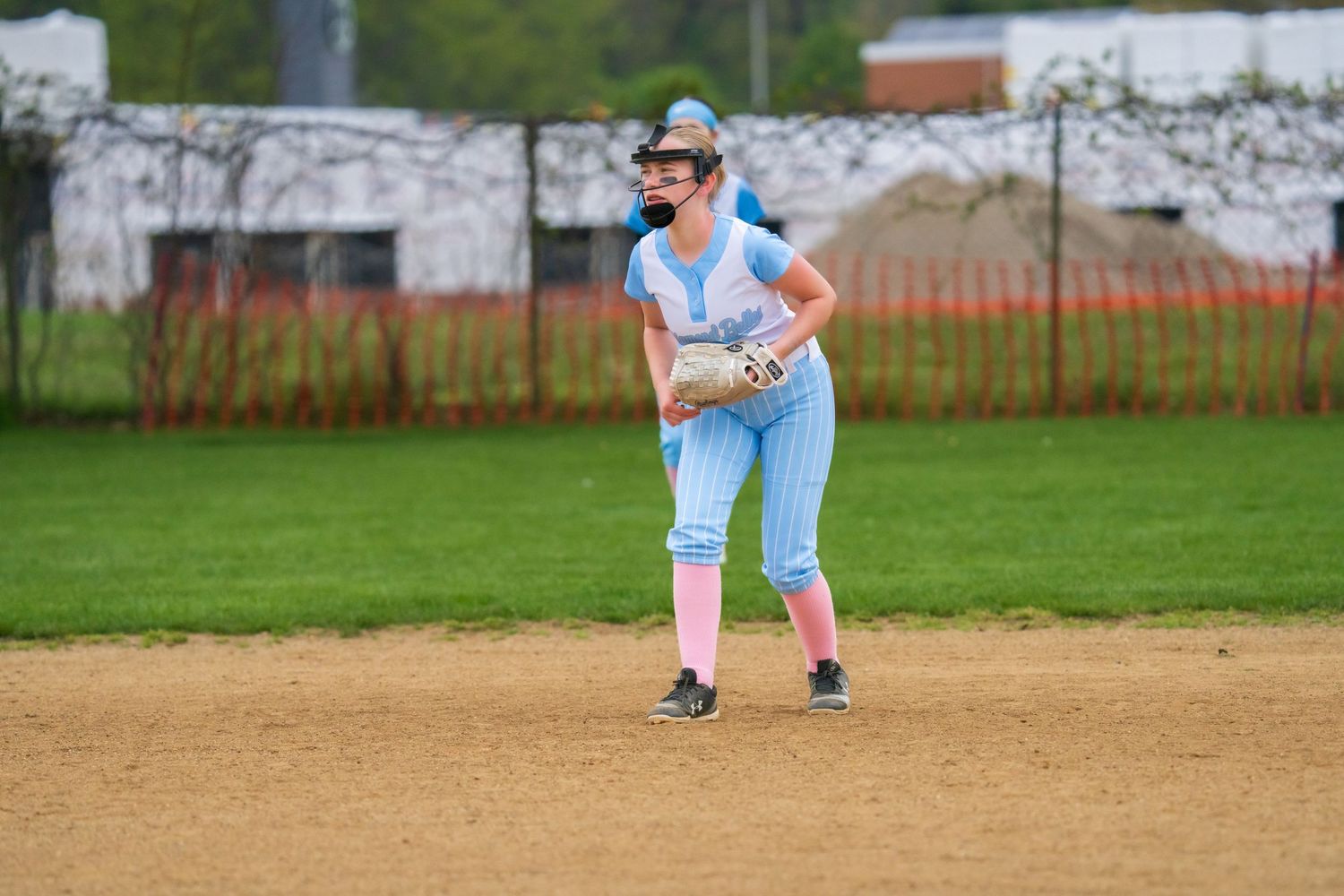 Female softball player in light blue uniform fielding a ball on a dirt infield during a game.