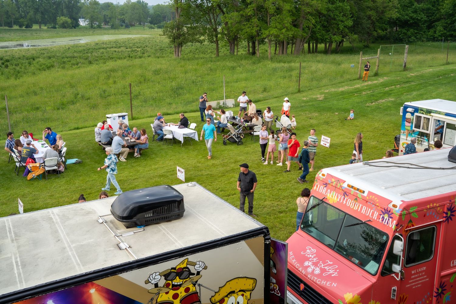Aerial view of a food truck festival with crowds gathered on green grass near colorful trucks.