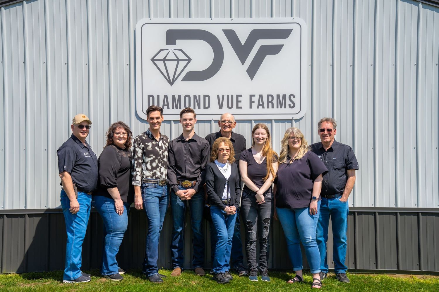 Group of nine people posing in front of Diamond Vue Farms barn sign on a sunny day.