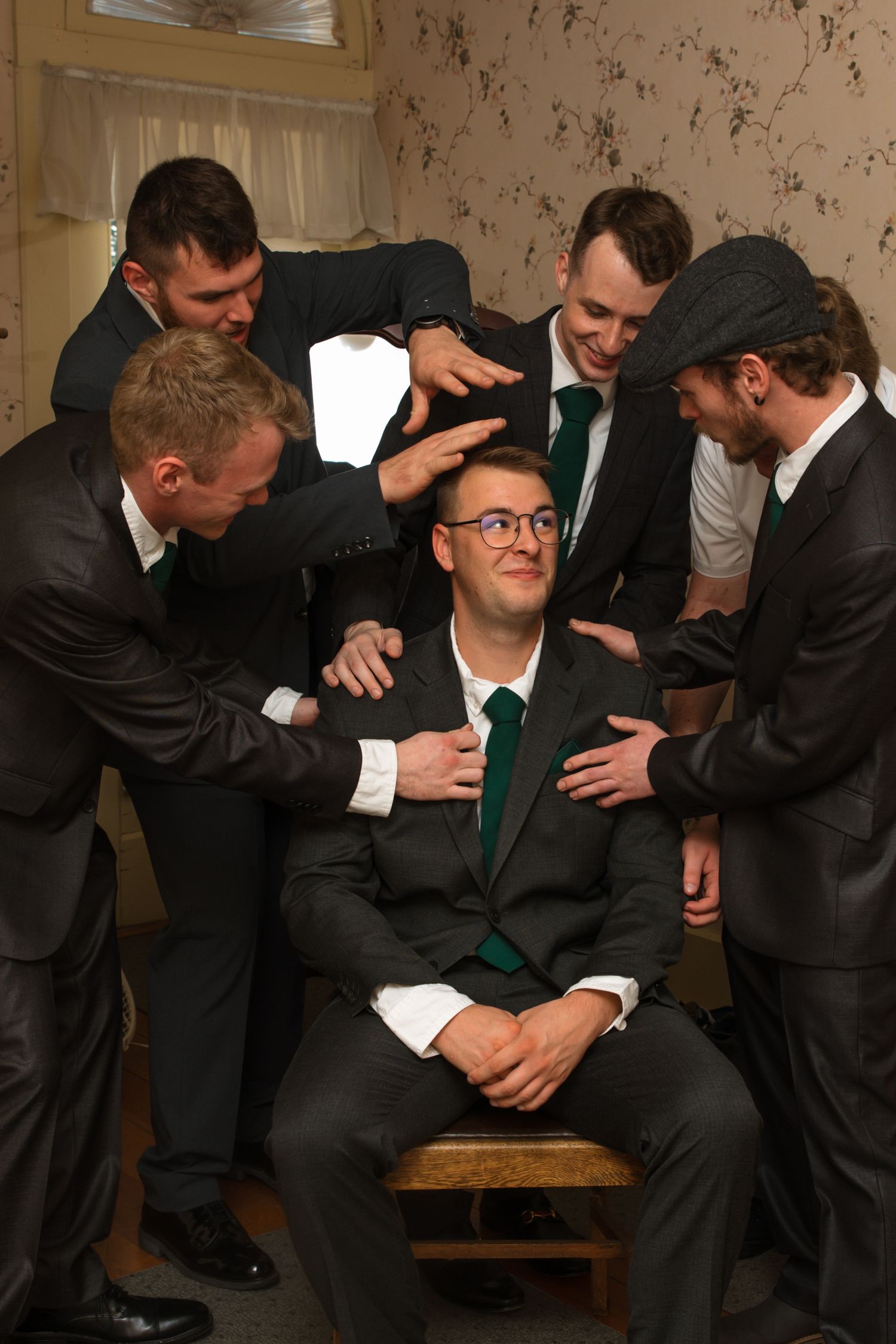 Groom sits smiling as groomsmen surround and celebrate him before the wedding ceremony.