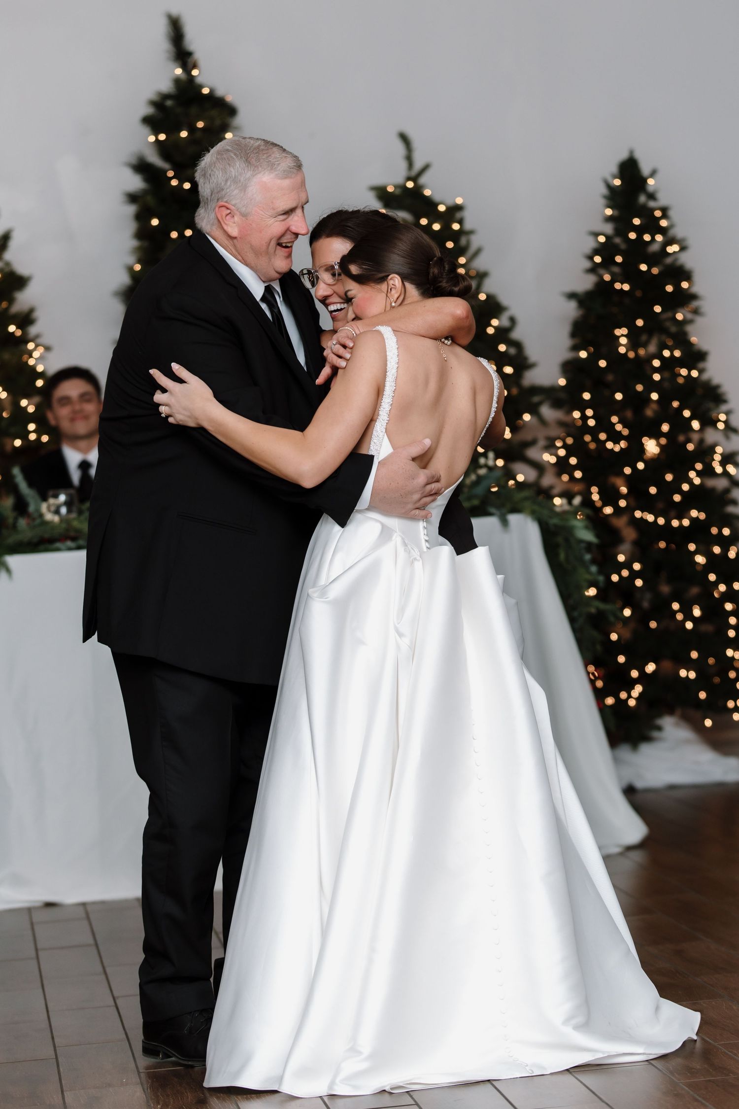 Bride shares a joyful father-daughter dance at wedding reception with festive Christmas tree backdrop.