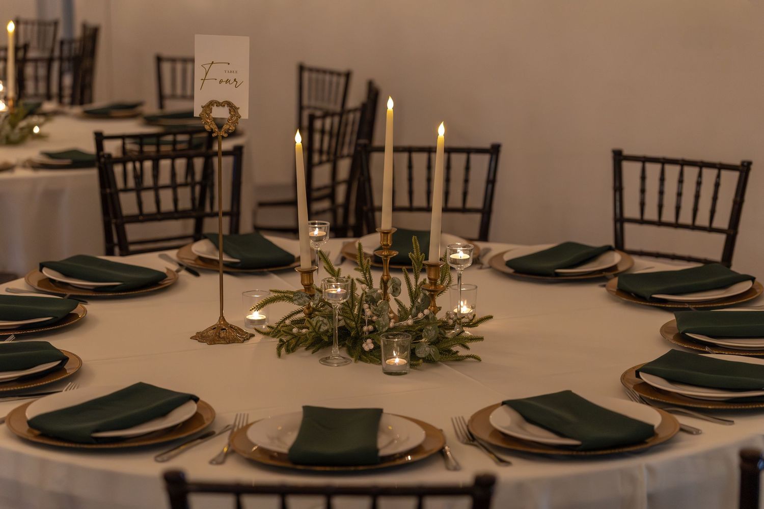 Elegant round wedding reception table with dark napkins, gold chargers, and candlelit centerpiece.