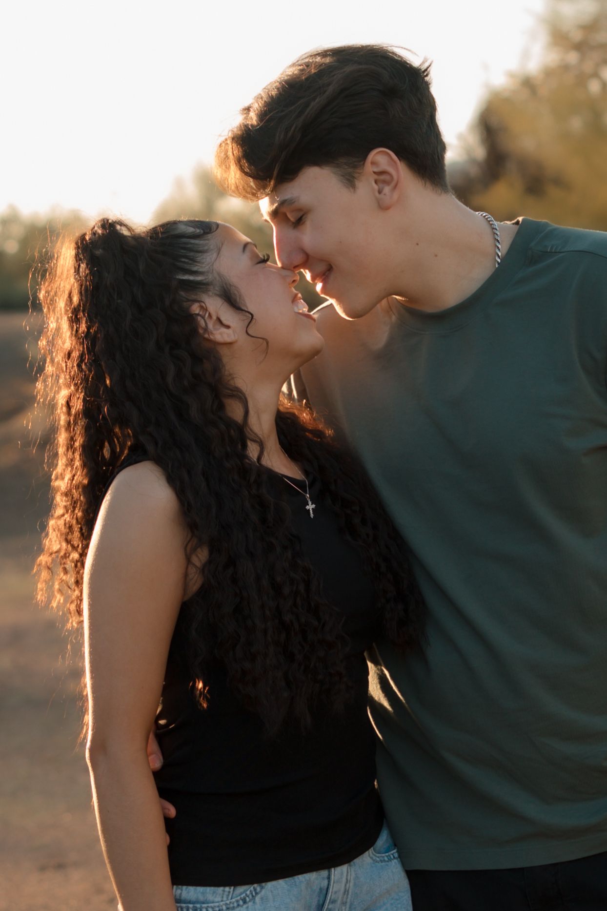Young couple leaning in for a kiss bathed in warm golden sunset light outdoors.