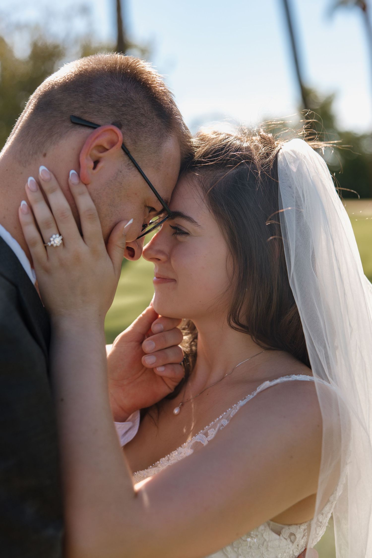 Bride and groom share an intimate forehead touch moment, bride wearing lace dress and veil with diamond engagement ring.