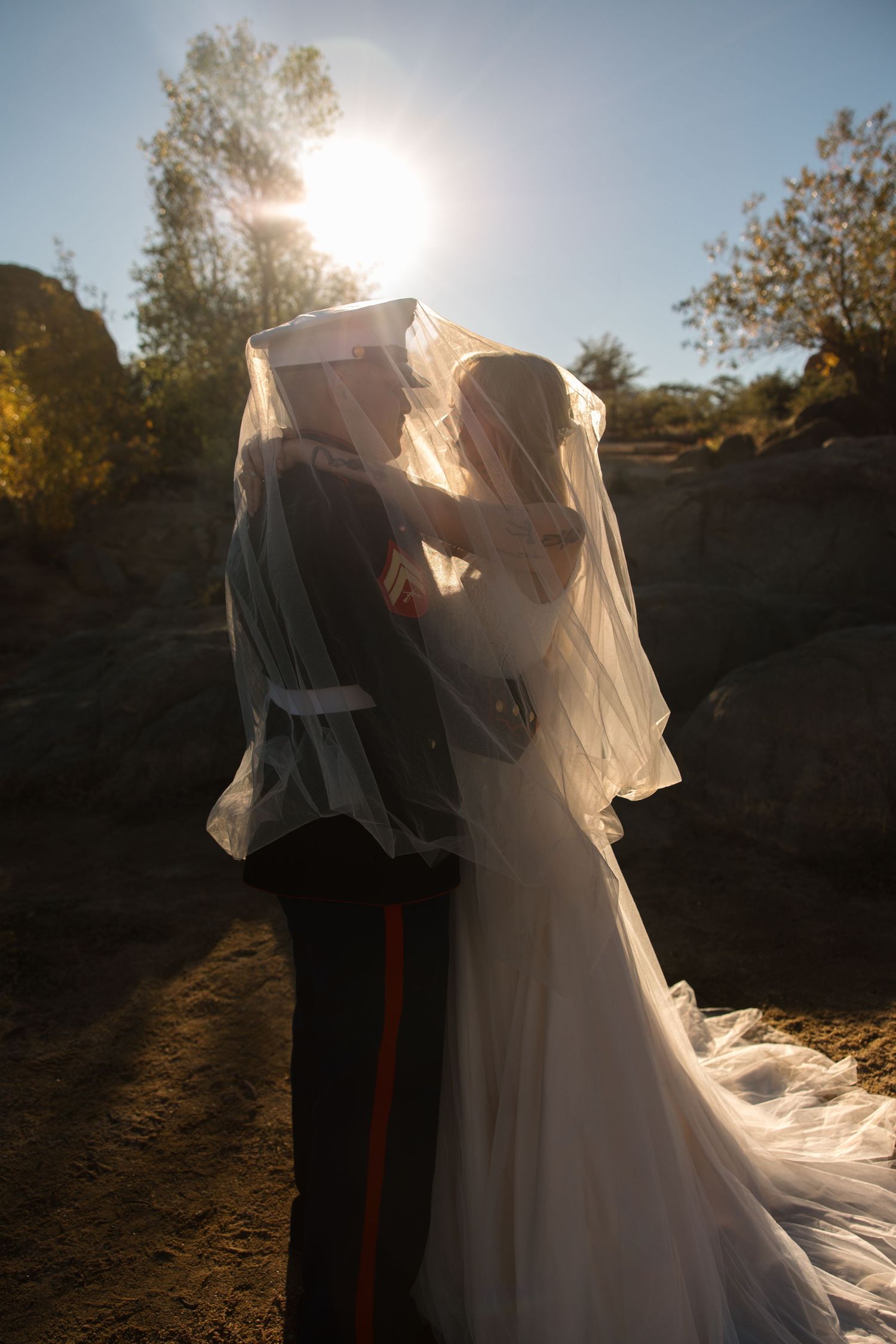 Bride and Marine groom share a kiss under flowing veil in golden sunlight.