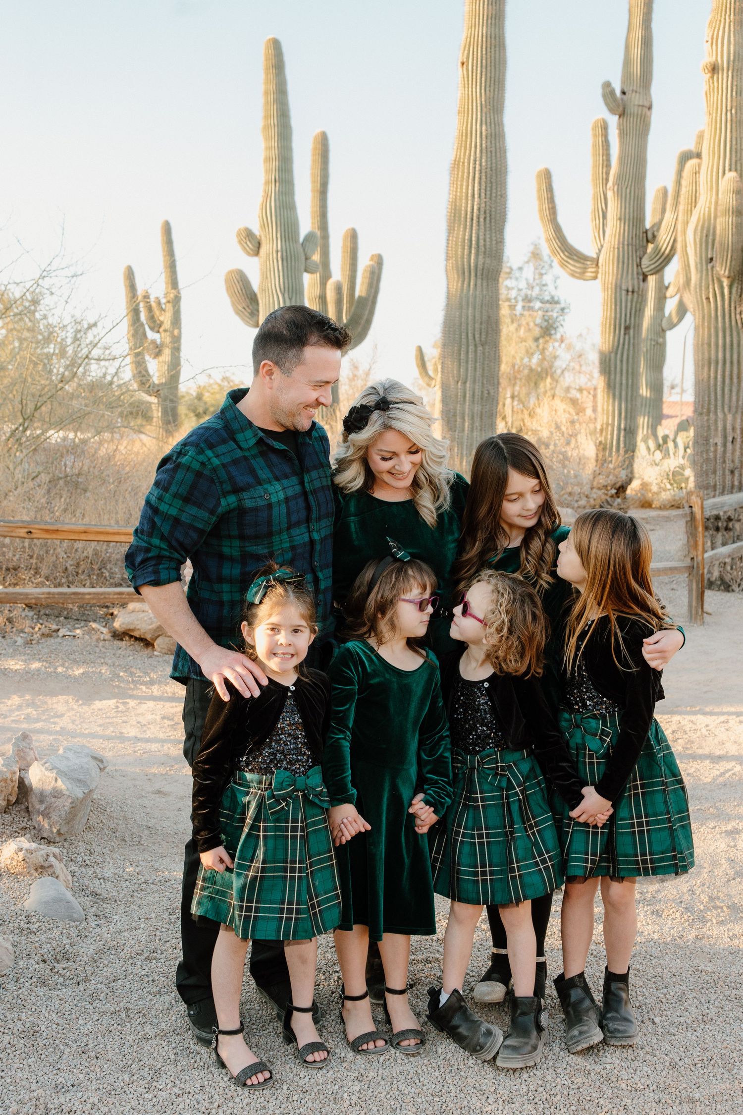 Family of six poses in matching green plaid outfits among saguaro cacti in Arizona desert setting.