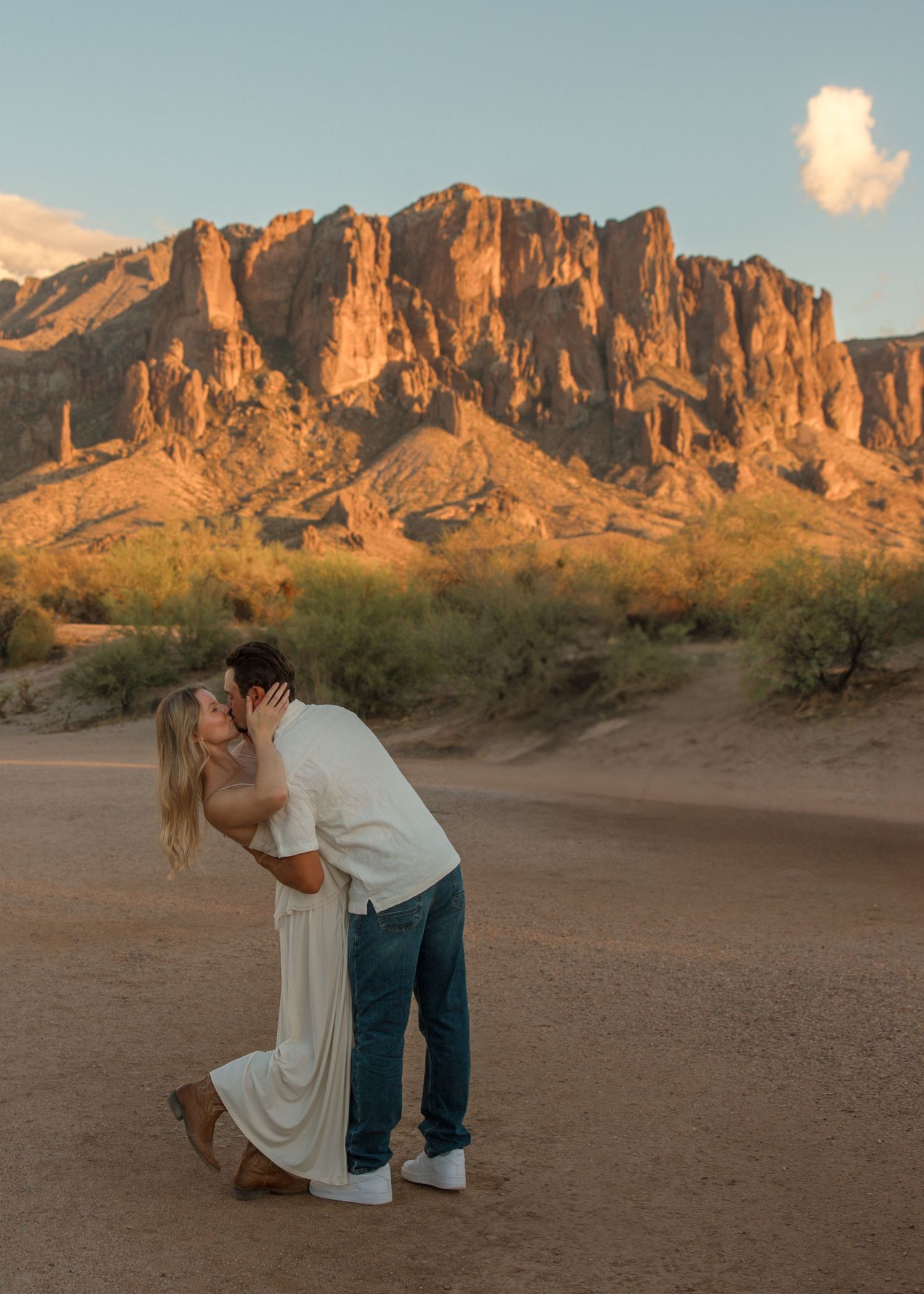 Couple sharing a romantic dip kiss in the desert with Superstition Mountains glowing at sunset in Arizona.