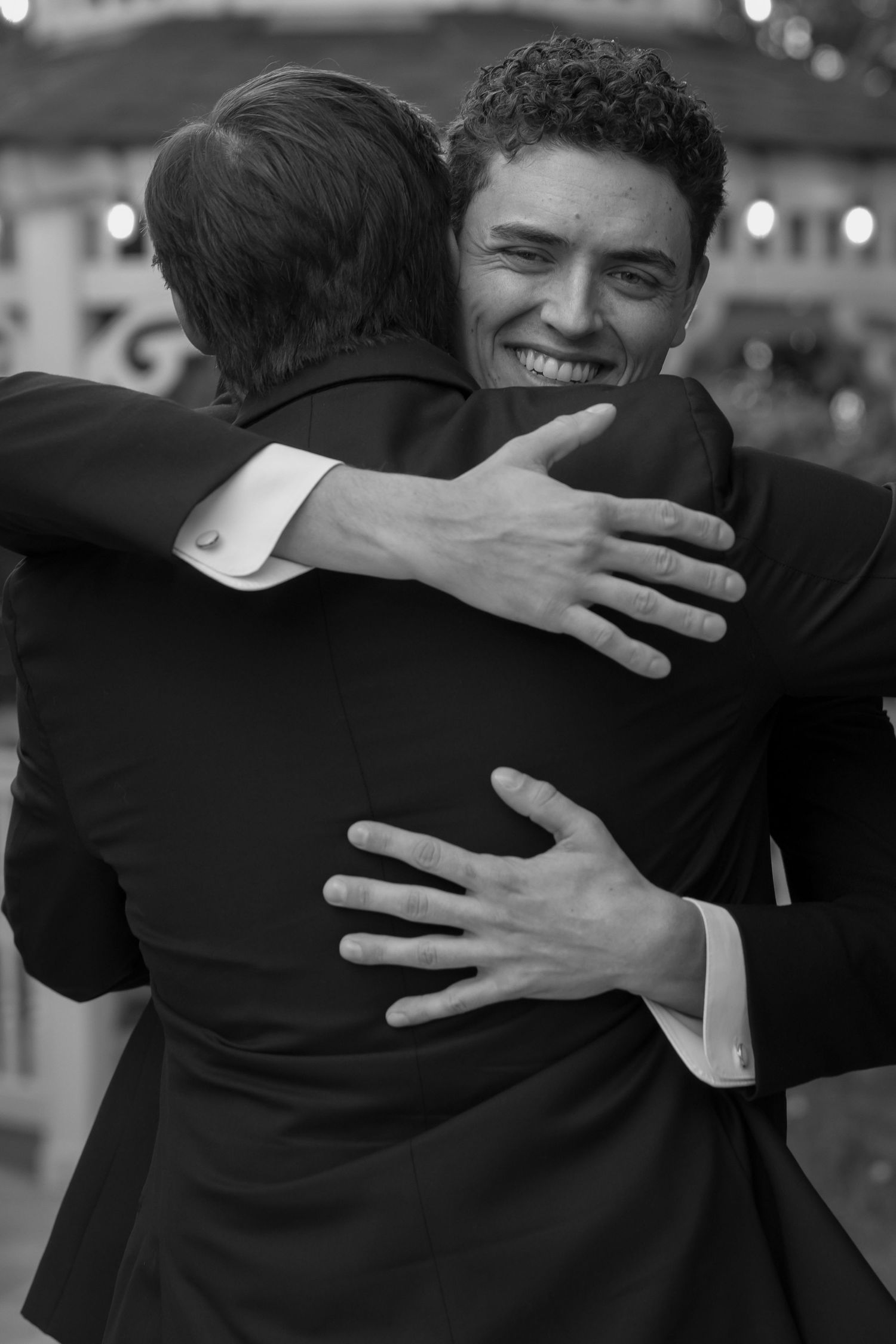 Black and white photo of groom sharing heartfelt hug with guest at outdoor wedding reception.