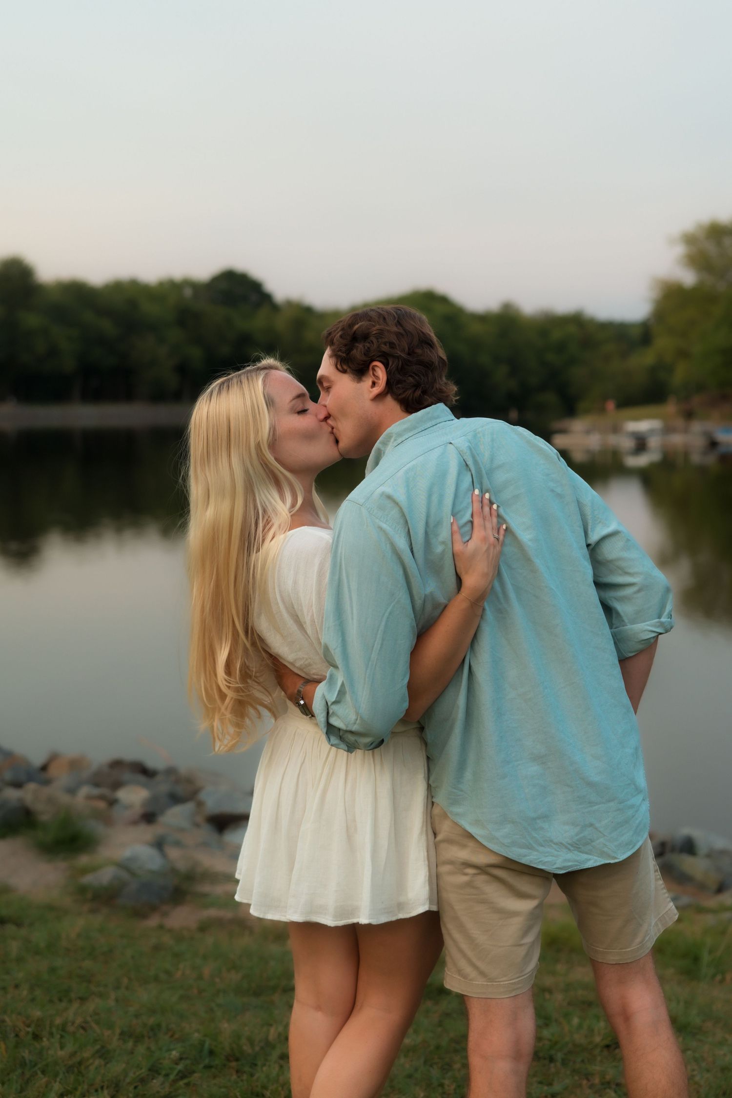 Young couple sharing a romantic kiss while standing by a scenic lake at dusk.