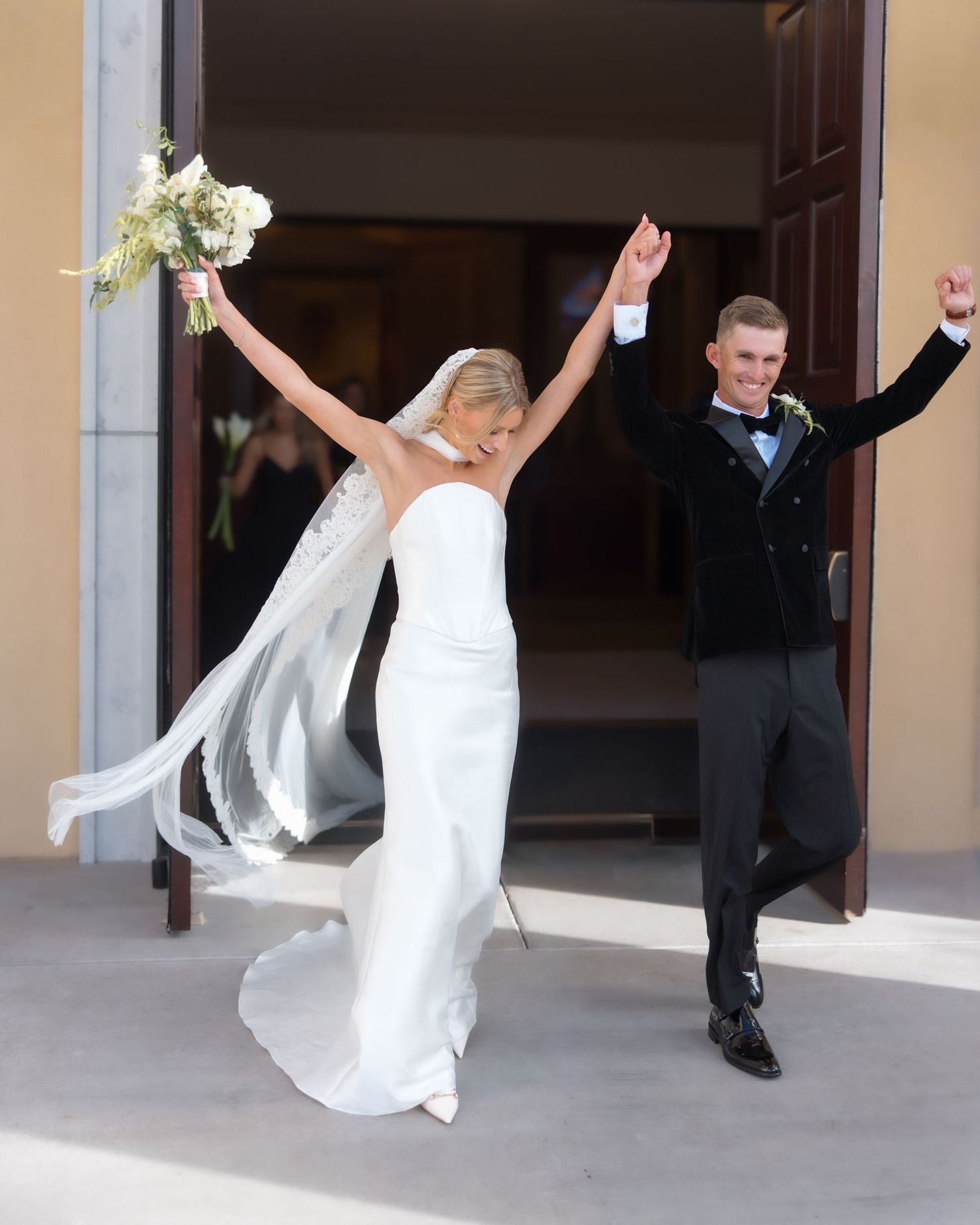 Jubilant newlyweds celebrating with raised arms as they exit church doors after wedding ceremony.