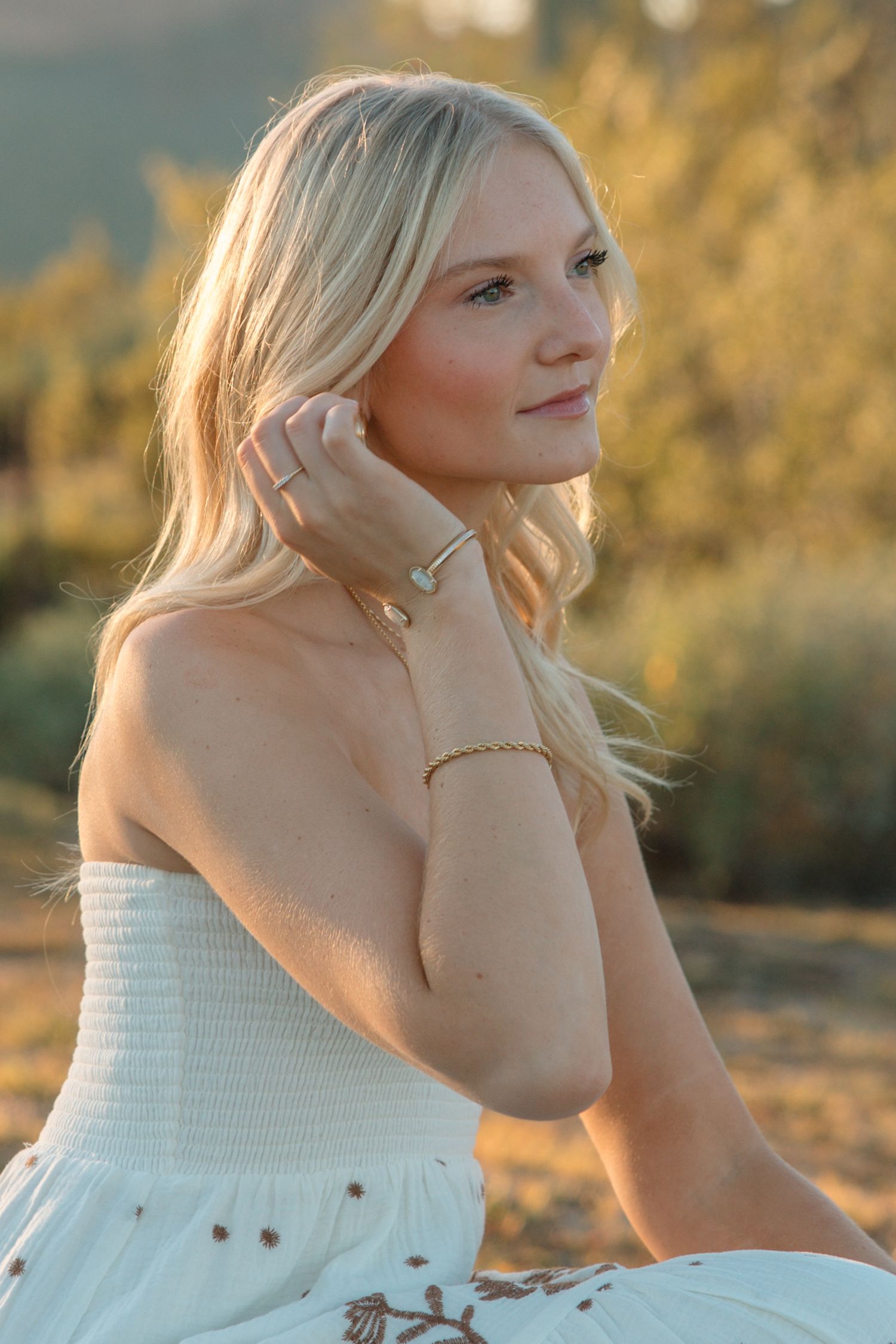 Close-up portrait of blonde woman in white strapless dress wearing gold jewelry in warm desert sunset light.