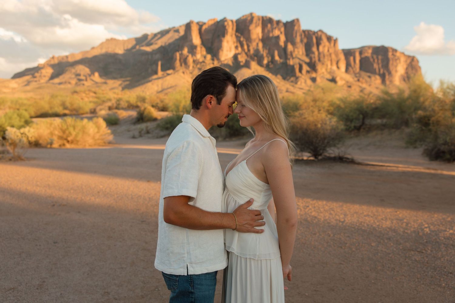 Couple sharing a romantic embrace in the desert with Superstition Mountains at golden hour in Arizona.