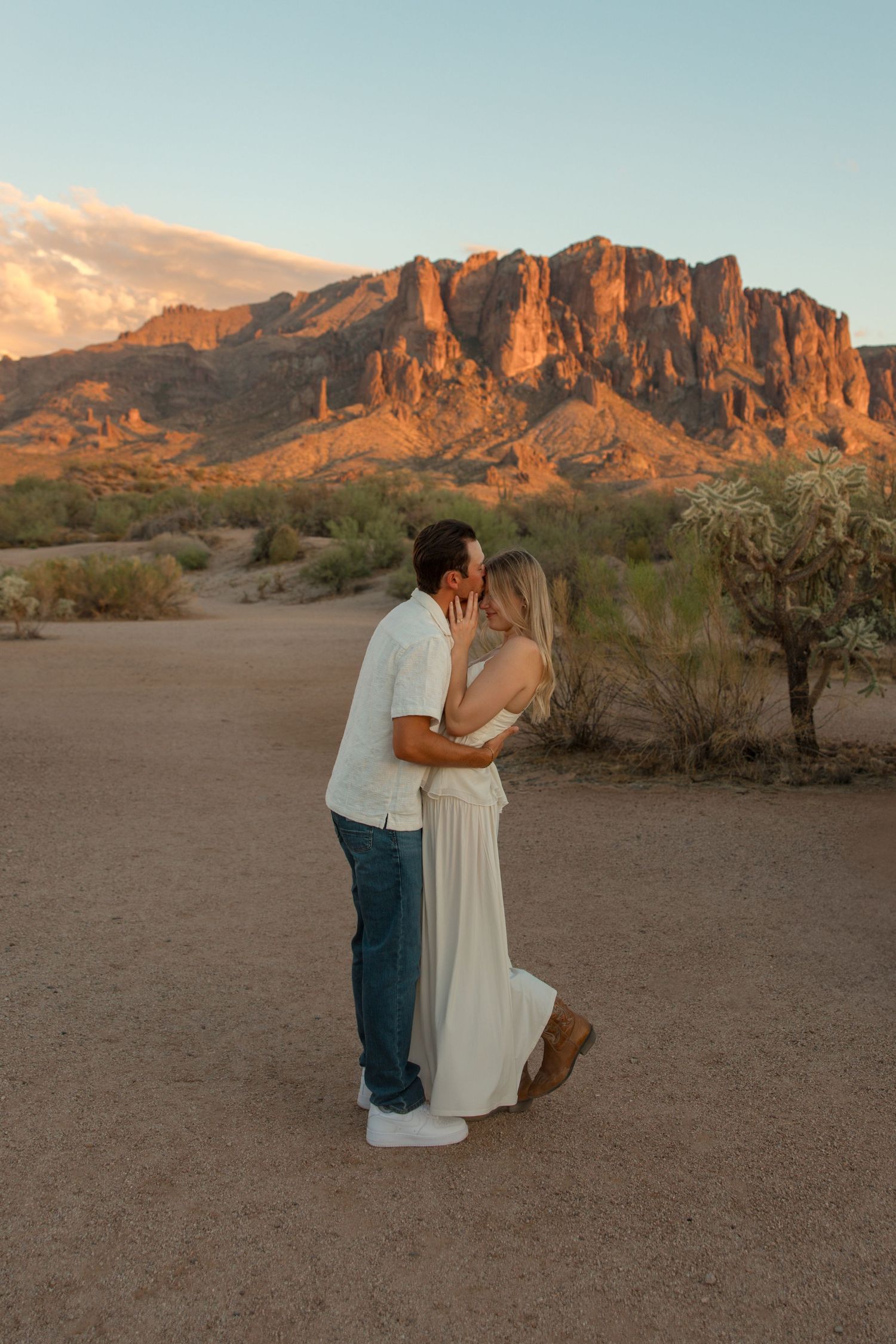 Couple sharing a kiss at sunset with Superstition Mountains glowing orange in the Arizona desert background.