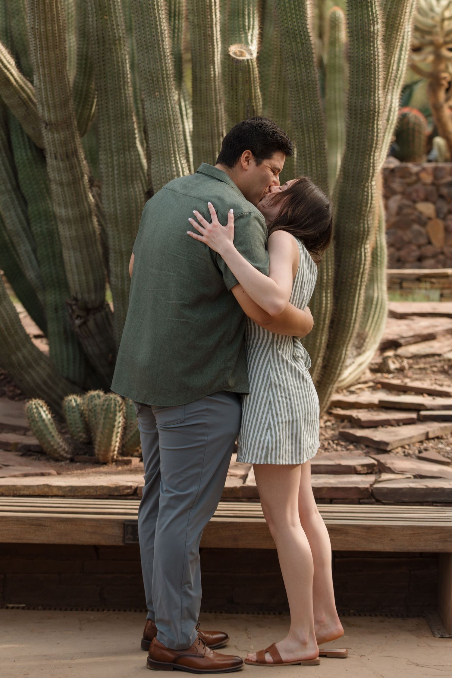 Couple sharing a romantic kiss in front of tall green cacti in a botanical garden setting.