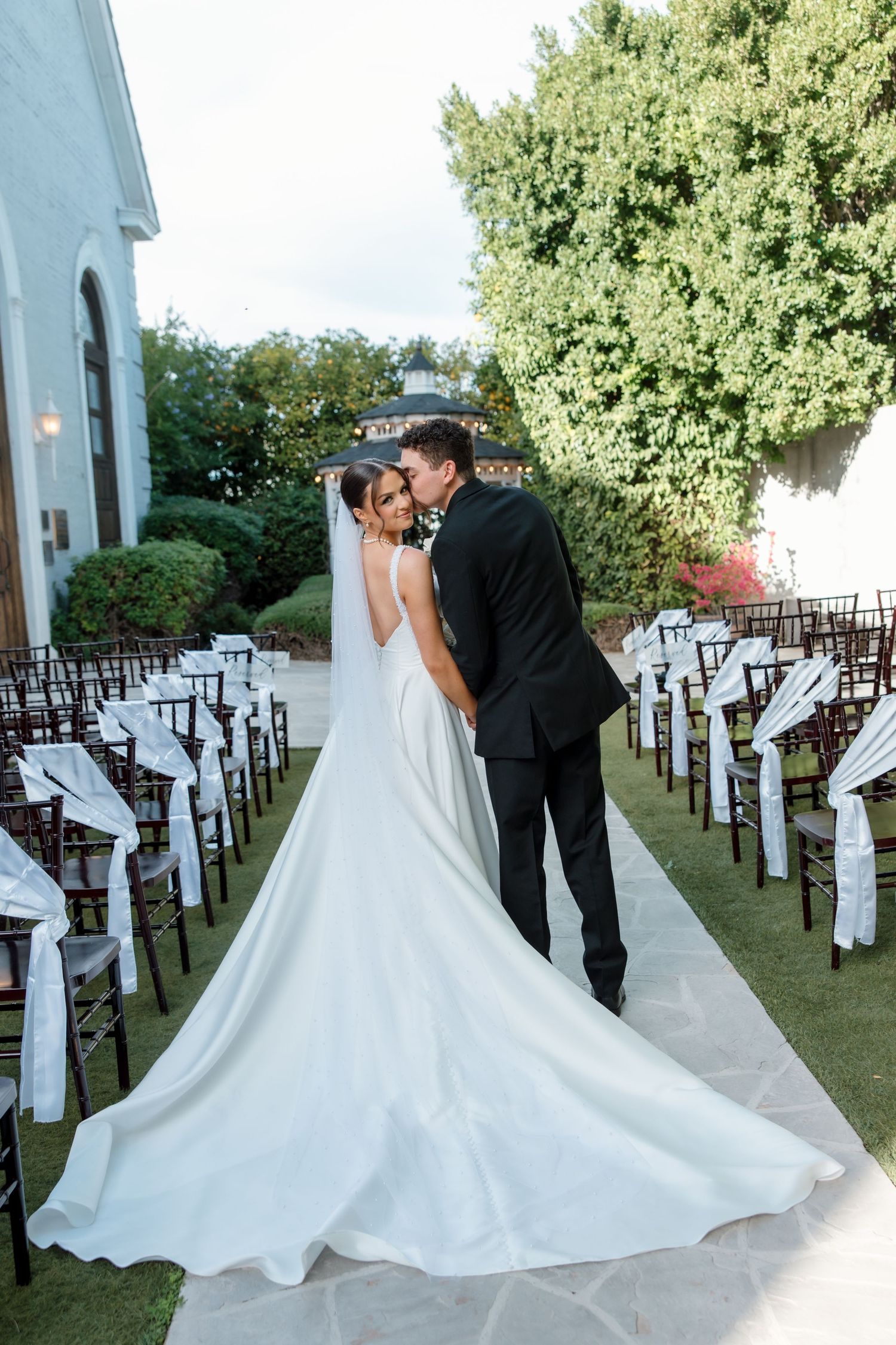 Bride and groom sharing a kiss from behind, showcasing the long cathedral wedding gown train.