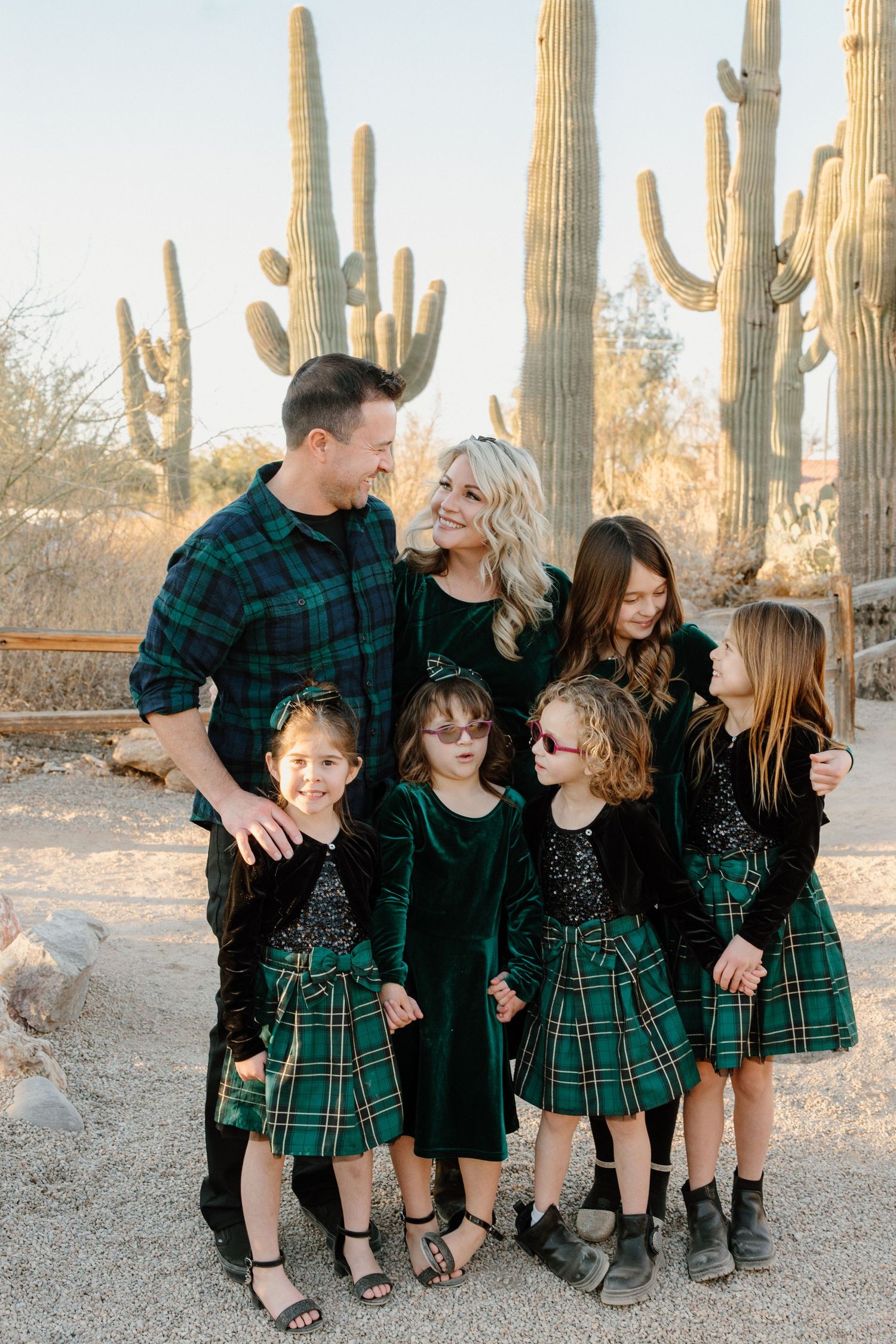 Family of six in coordinating green plaid and velvet outfits posing among tall saguaro cacti in Arizona desert.
