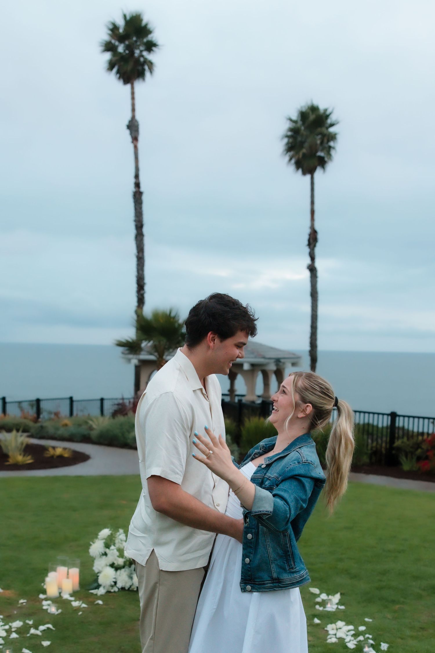 Happy couple embracing and gazing at each other in a coastal garden with palm trees and ocean view.