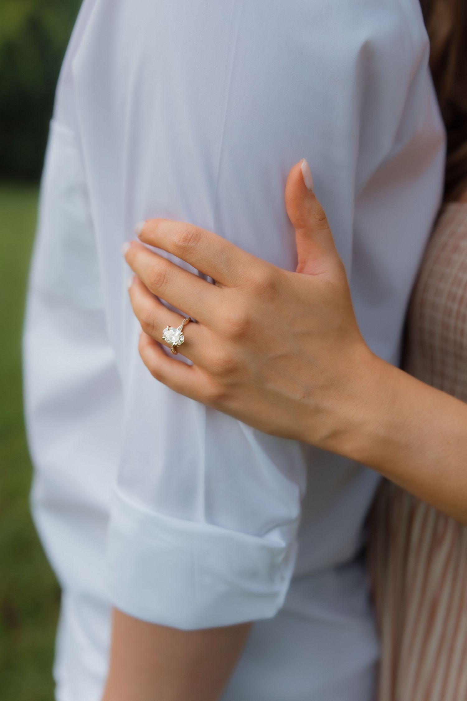 Close-up of a woman's hand wearing a gold diamond engagement ring resting on a man's white dress shirt.