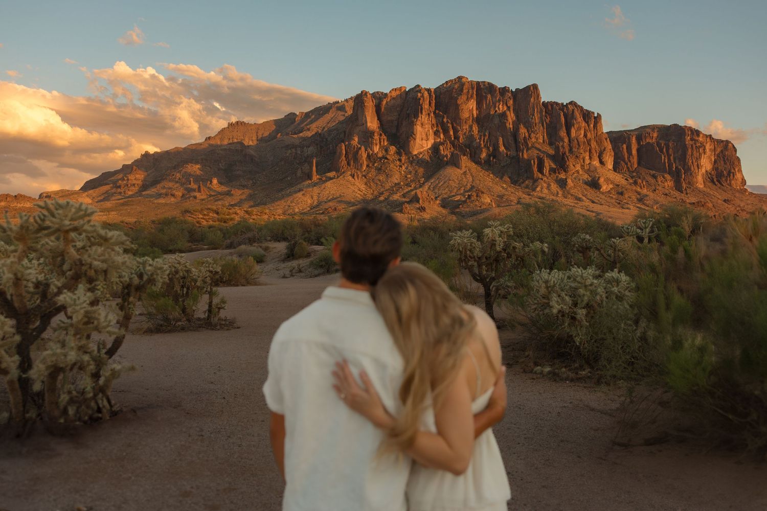 Couple embracing while gazing at Superstition Mountains in Arizona desert at golden sunset hour.