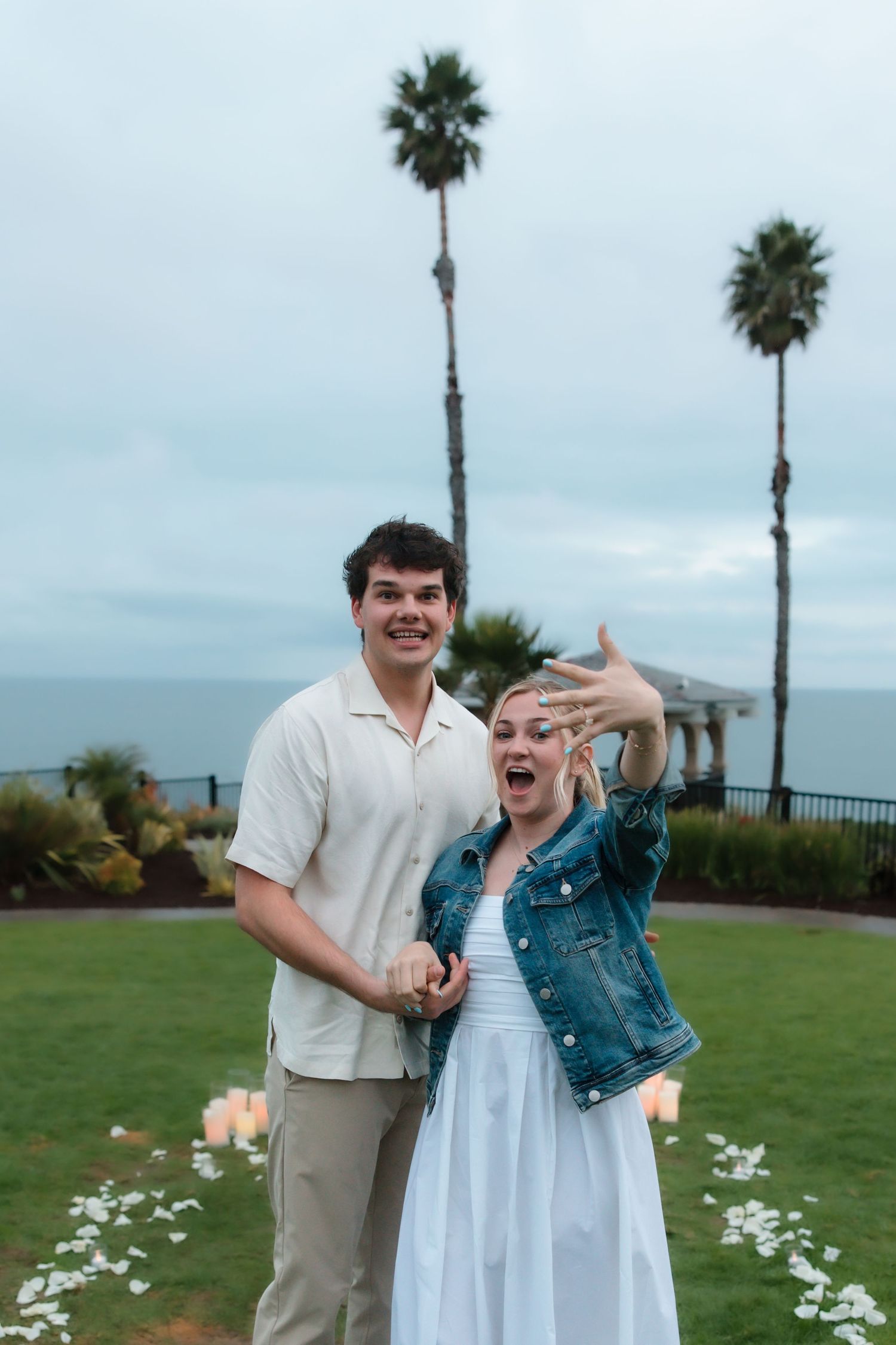 Excited newly engaged woman showing off her ring while smiling with her fiance outdoors.