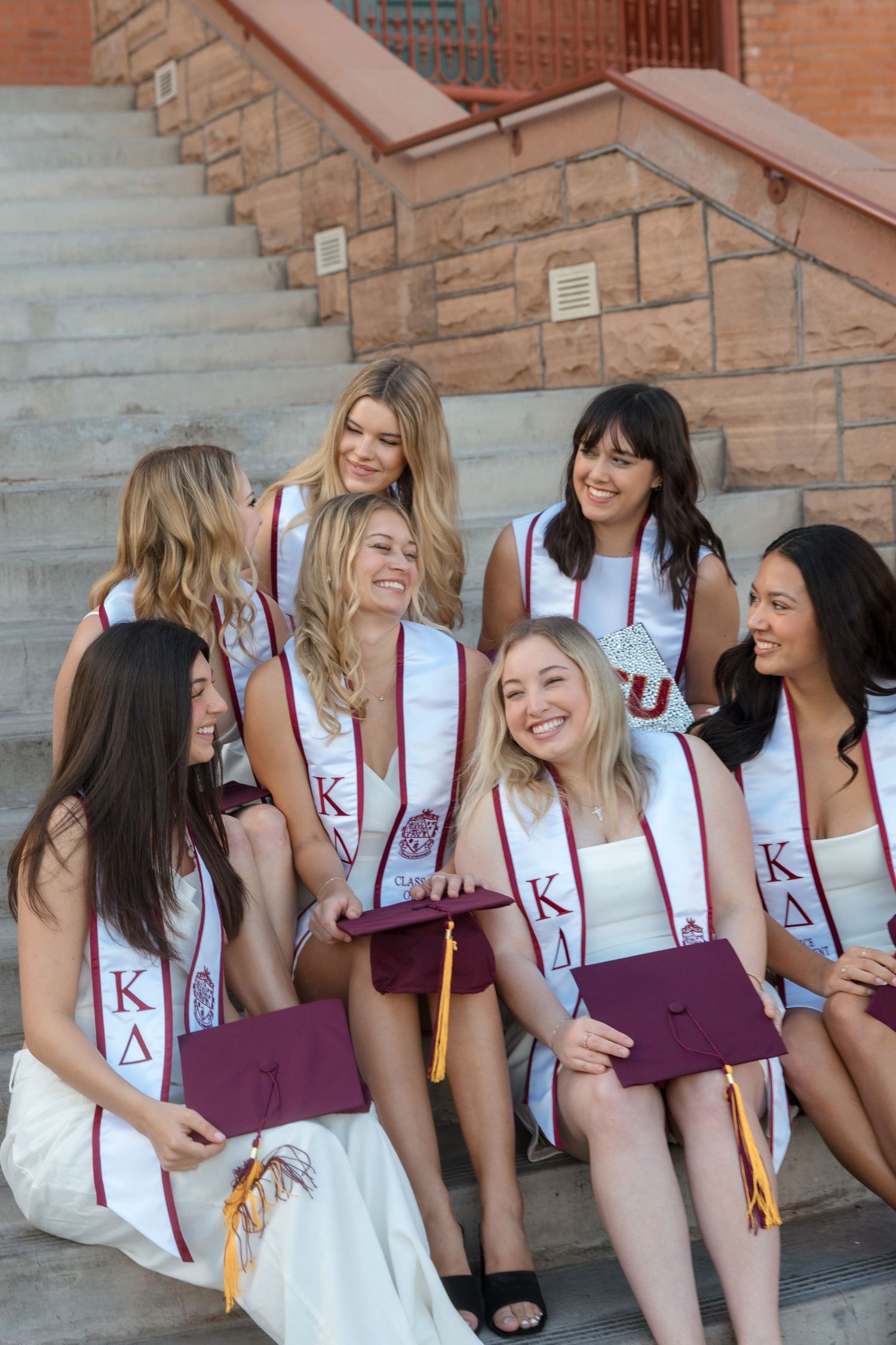 Group of college women in Kappa Delta sorority stoles celebrating graduation on university steps.