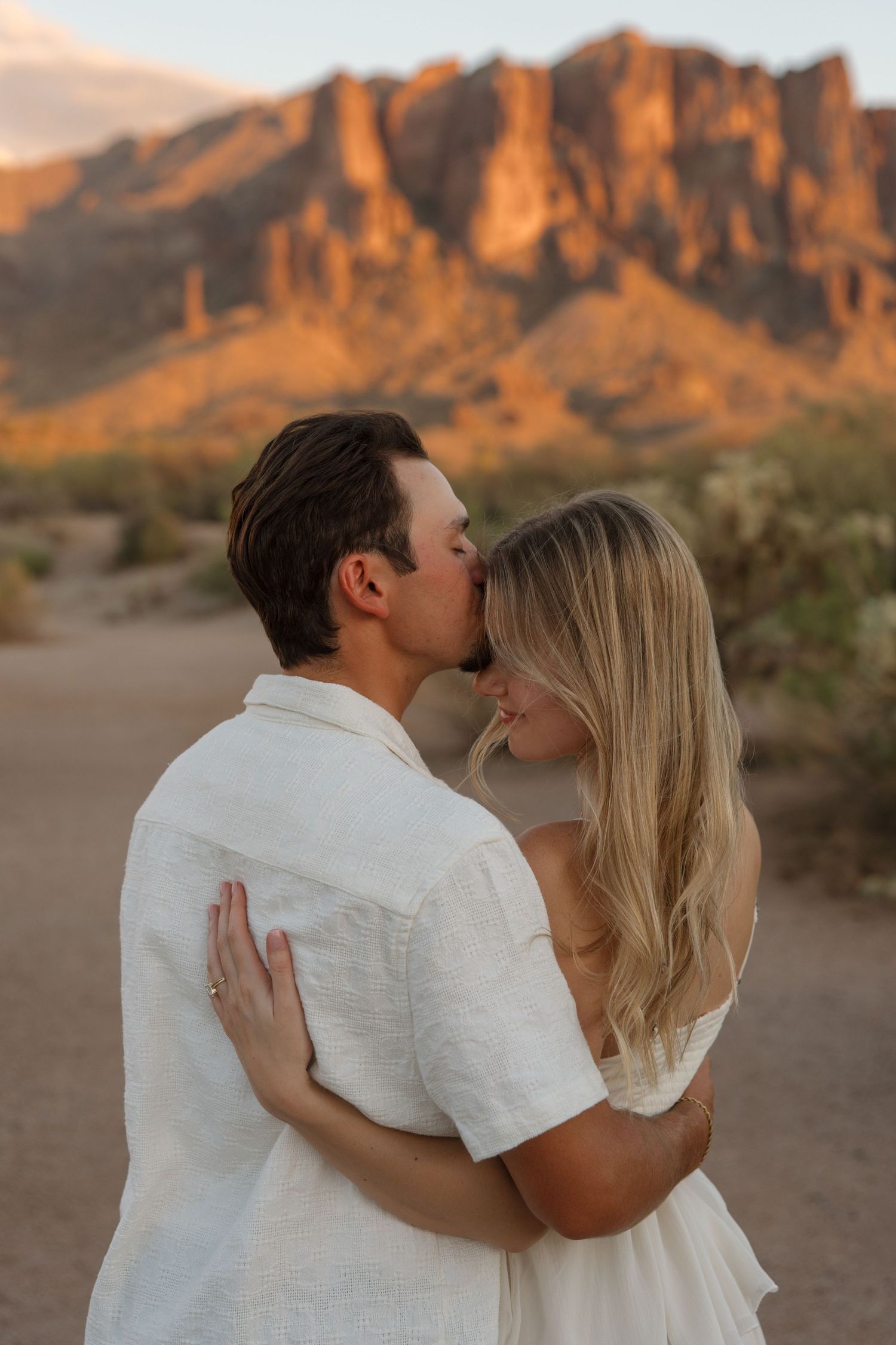 Couple sharing a kiss at sunset with Superstition Mountains in the Arizona desert background.