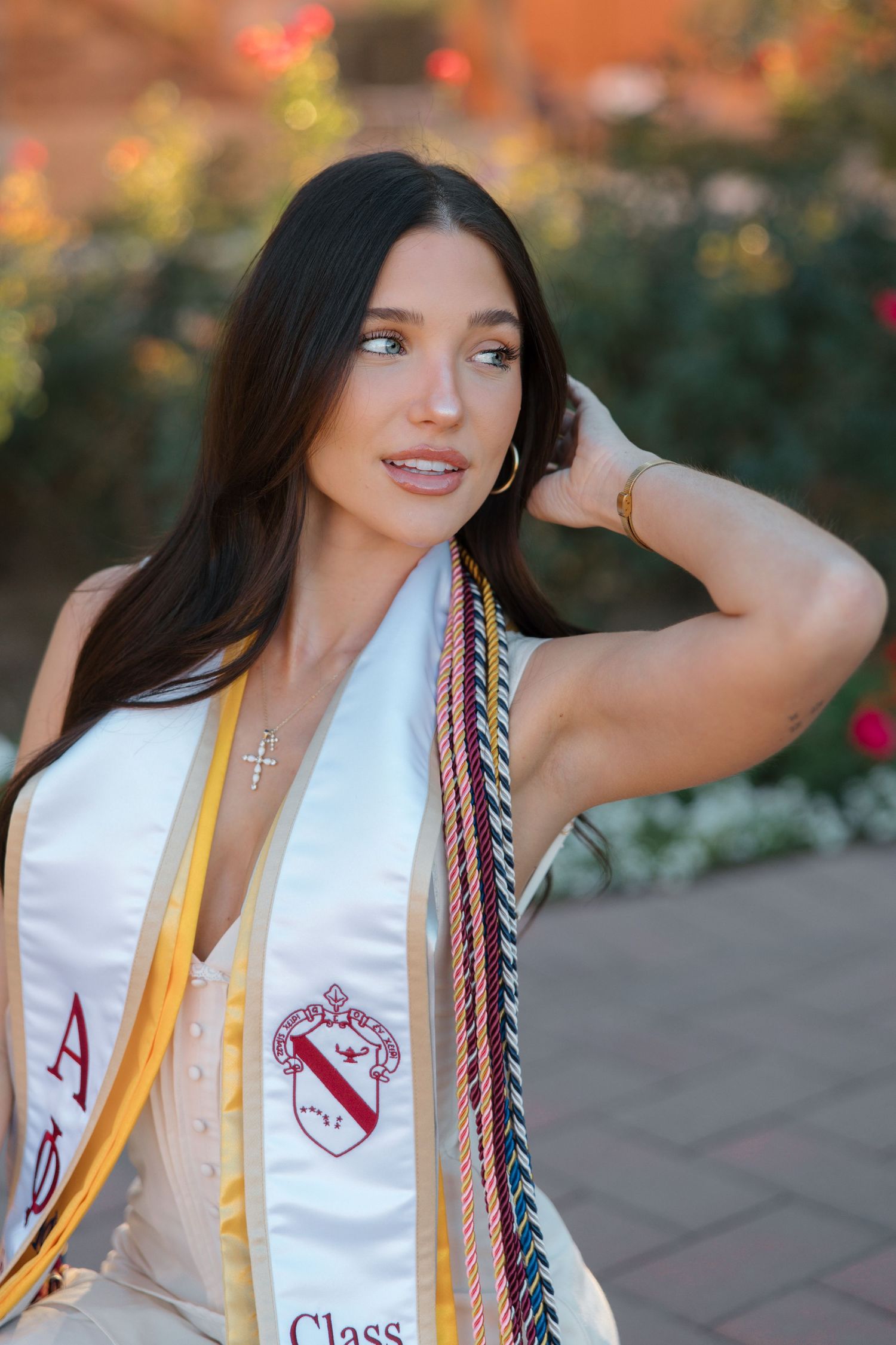 Young brunette woman in Alpha Phi graduation stole with multicolored honor cords looks away.