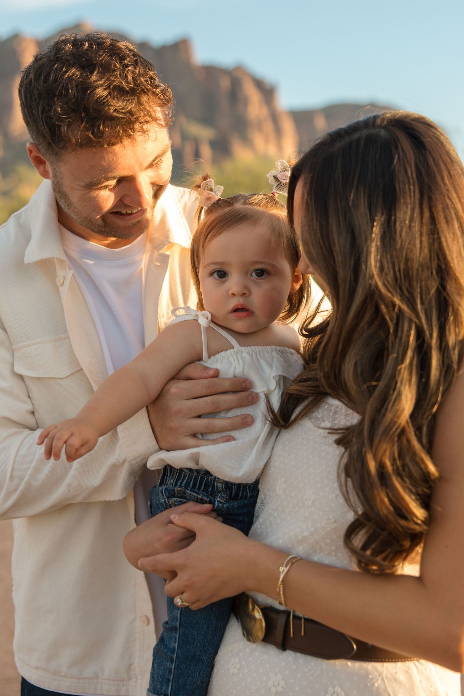 Parents lovingly holding their toddler daughter in a scenic desert mountain setting at golden hour.